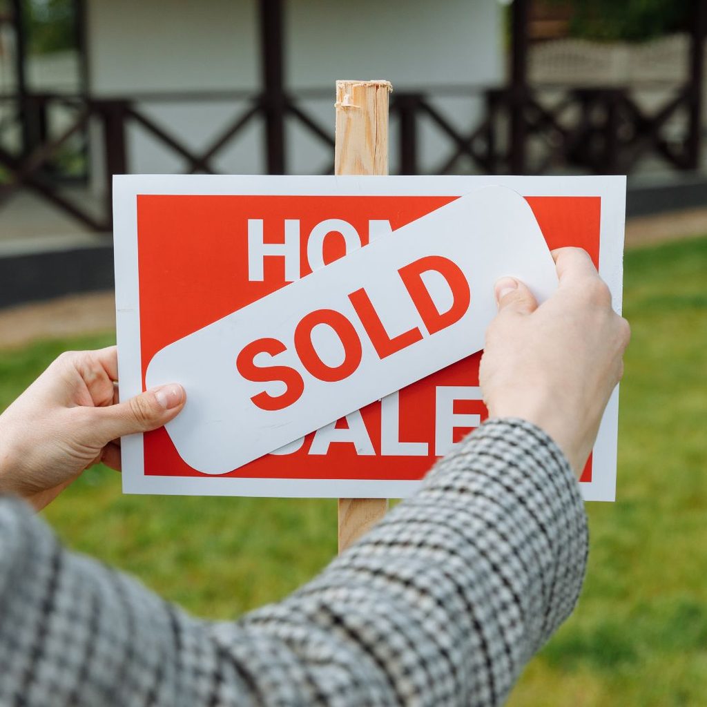Person places 'sold' sign over a 'for sale' sign outside a house