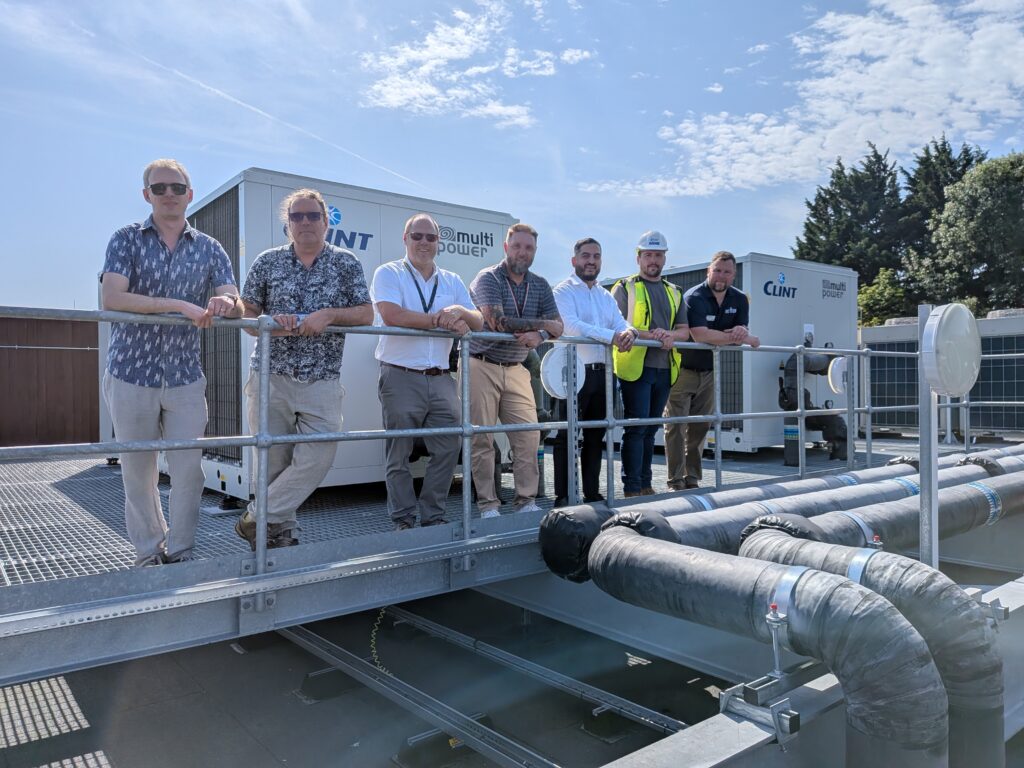 men stanbding in front of two air source heat pumps on roof of building