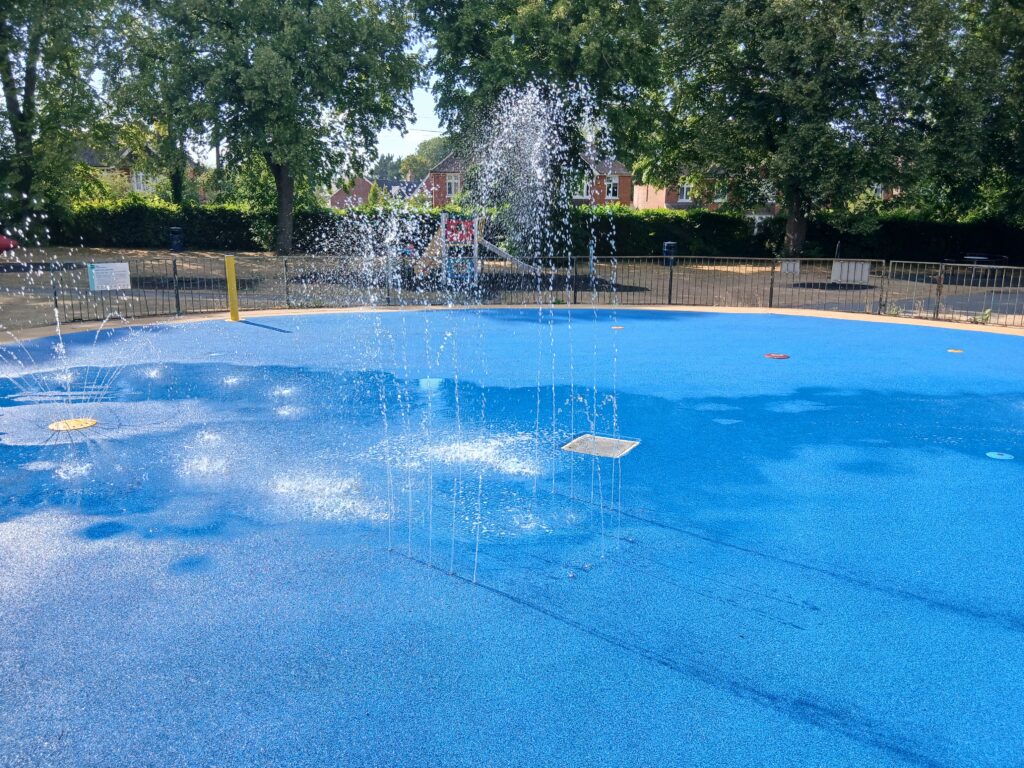 blue splash pad surrounded by trees with water fountain