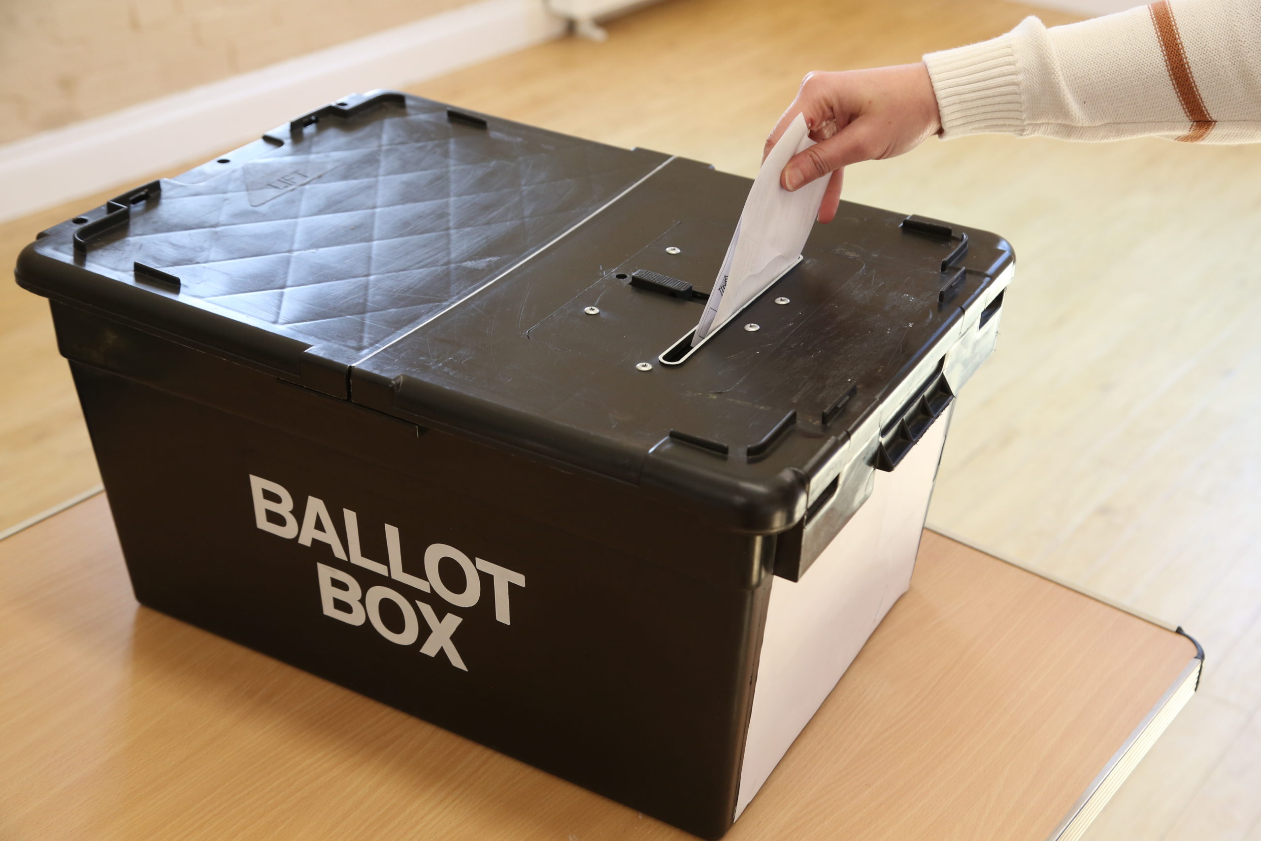 A photo of someone's arm posting a paper into a ballot box